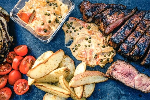 Entrecôte grillée en tranches, de la sauce, des frites et des tomates cerise sur un fond presque noir.