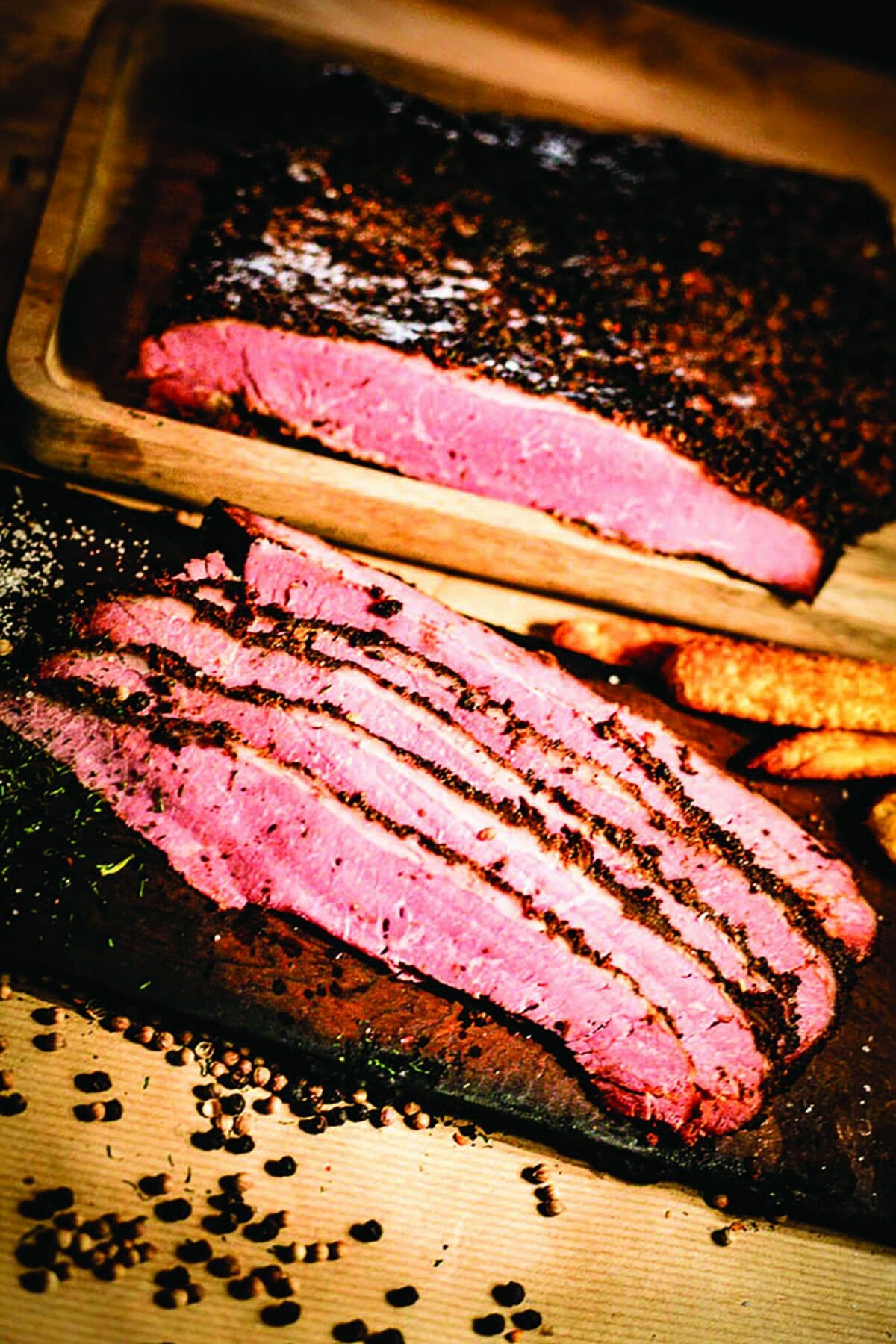 Des tranches fines de pastrami sur du papier boucher, un pastrami dans le fond.