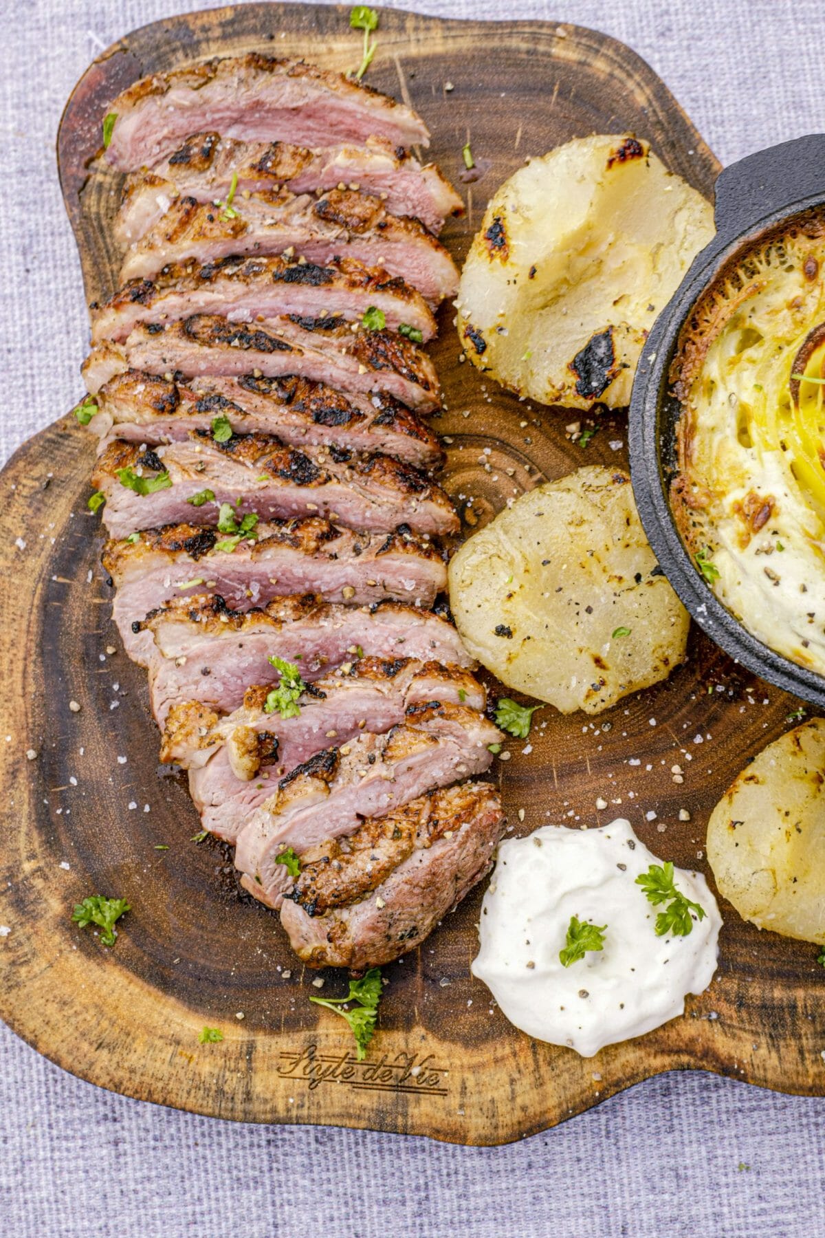 Sur une planche en bois, un filet de canard grillé et tranché, 2 demi poires, un peu de mousse de poires et un gratin dauphinois