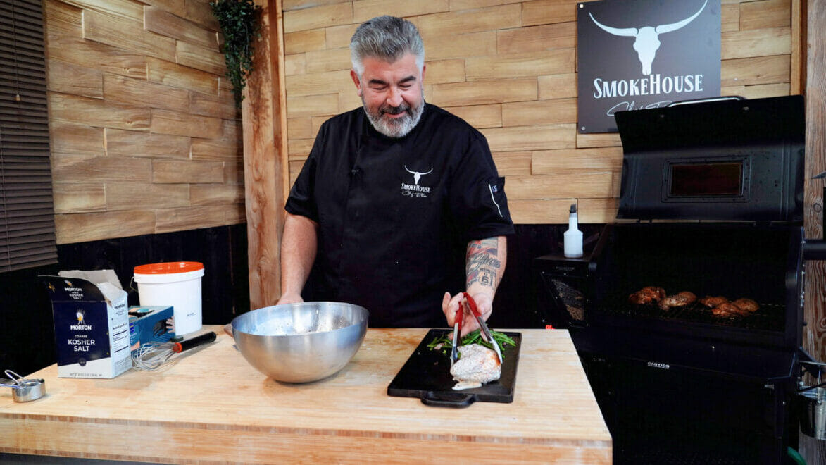 Chef Rohan sur son plan de travail en train de sortir les cuisses de poulet Big Bob Gibson de la sauce et les mettre sur une plancha