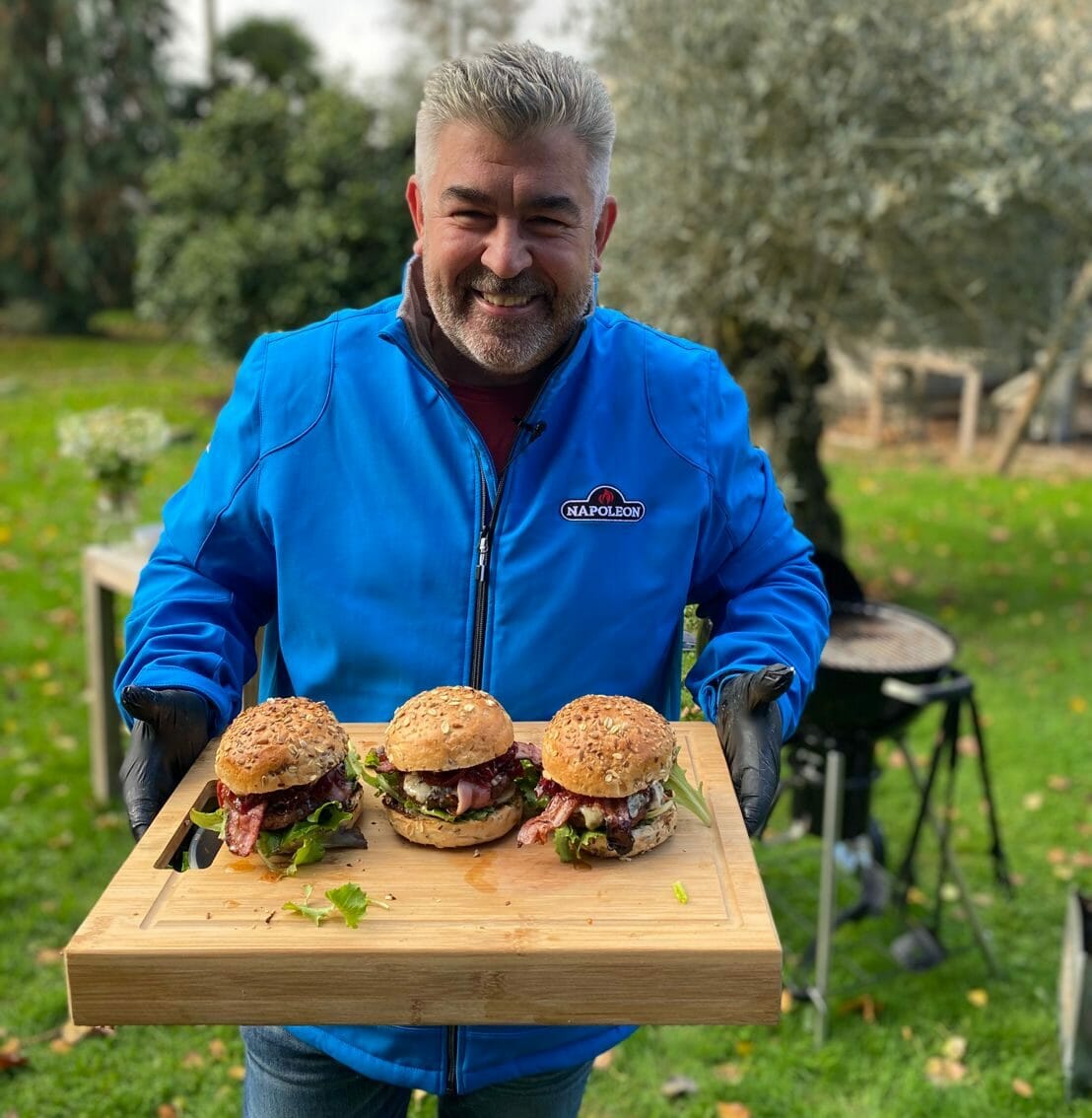 Chef Rohan souriant tient une planche avec 3 burgers