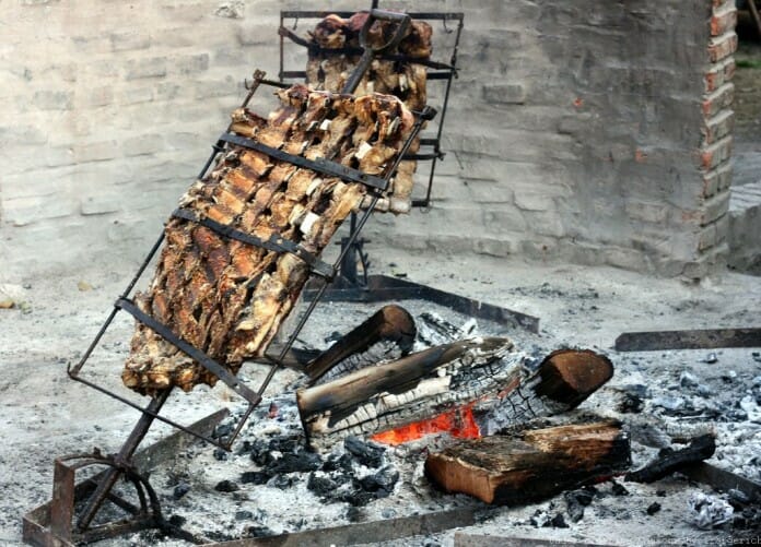 Asador a la Cruz avec de la viande dessus, au-dessus d'un feu de bûches de bois.