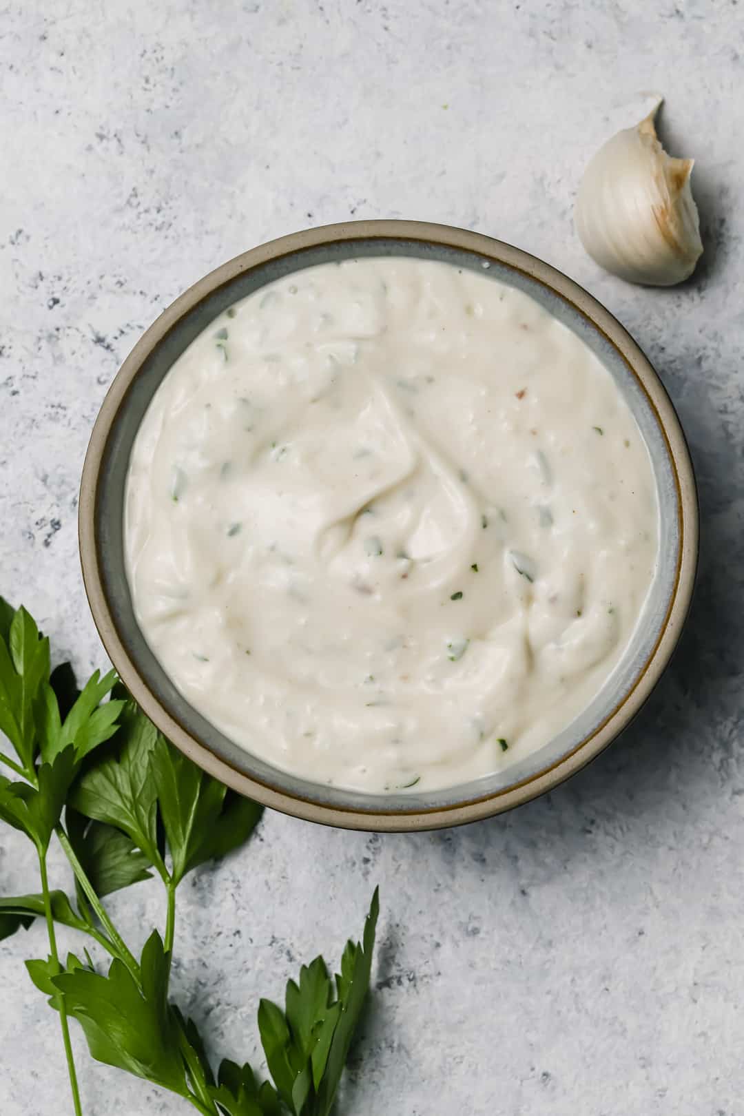 Un pot de sauce César vu de haut sur une pierre en marbre avec une branche de persil plat.