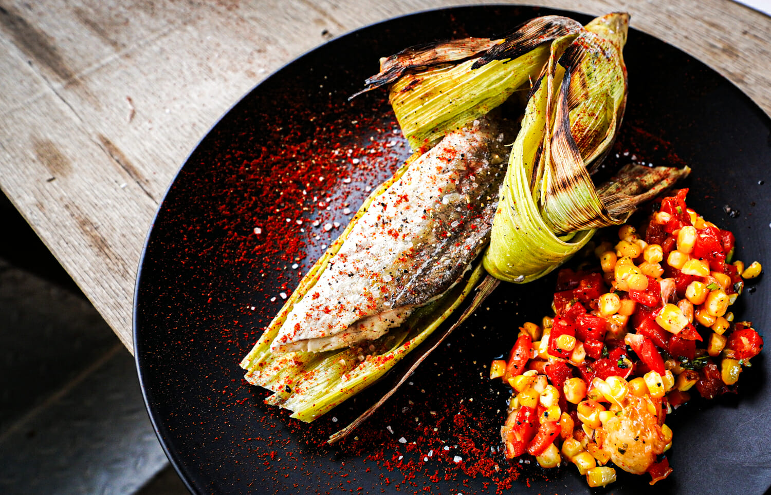 morceau de poisson dans un épi de maïs, salade maïs et poivrons sur le côté.