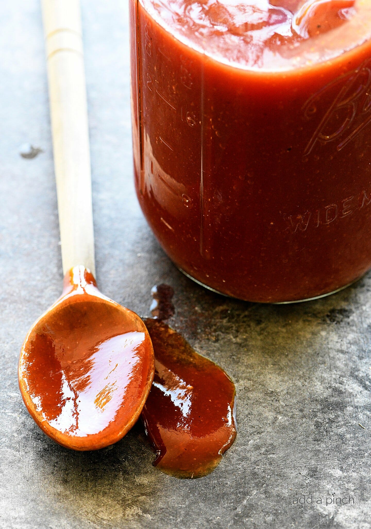 Une jarre Ball contenant de la sauce BBQ. avec une cuillère en bois sur le côté pleine de sauce.