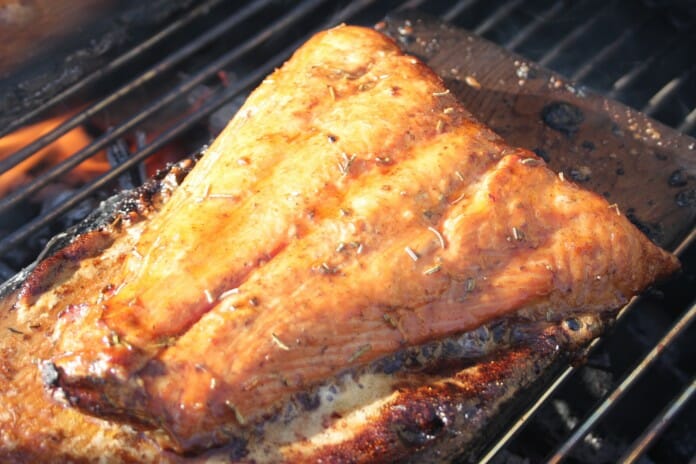 Un morceau de saumon caramélisé sur une planche de cèdre sur une grille de BBQ en flammes.