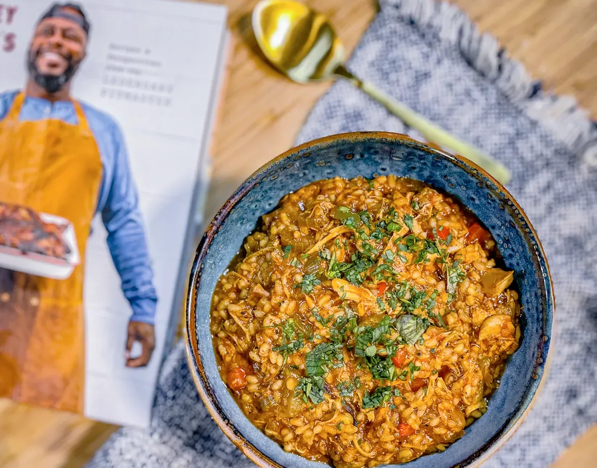 Un assiette bleue remplie du plat de chicken perloo de Rodney Scott avec à gauche le livre de Rodney Scott